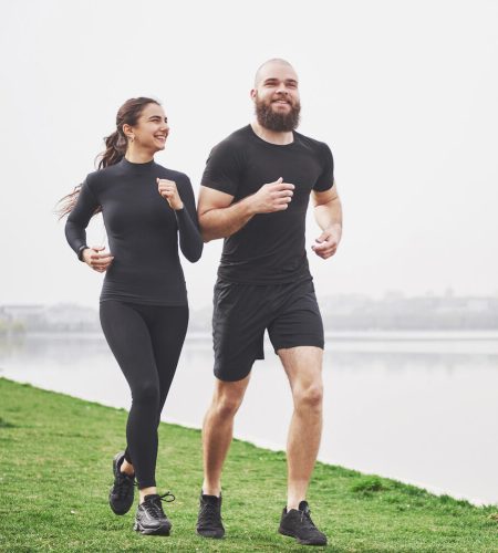 Couple jogging and running outdoors in park near the water. Young bearded man and woman exercising together in morning.